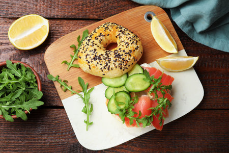 Delicious bagel with salmon, cucumber, arugula and lemon on wooden table, flat layの写真素材