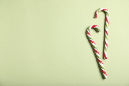 Tasty candy canes on green background, flat lay with space for text. Christmas treatの写真素材