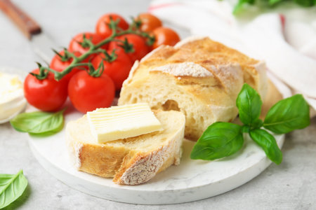 Slices of baguette with butter, basil and tomatoes on light gray table, closeupの写真素材