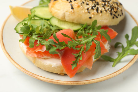 Delicious bagel with salmon, cucumber and arugula on white table, closeupの写真素材