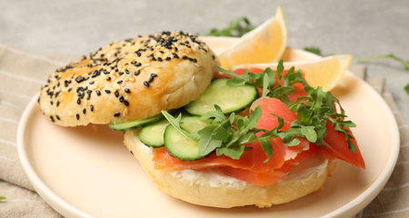 Delicious bagel with salmon, cucumber, arugula and lemon on table, closeupの写真素材