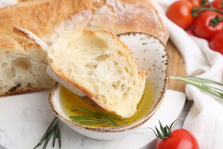 Tasty baguette served with oil, tomatoes and rosemary on table, closeupの写真素材