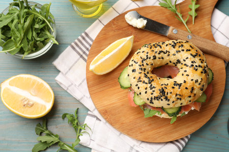 Delicious bagel with salmon, cream cheese, cucumber, arugula and lemon on light blue wooden table, flat layの写真素材