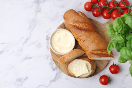 Cut baguette with butter, basil and tomatoes on white marble table, flat lay. Space for textの写真素材