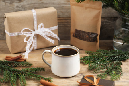 Aromatic coffee in cup, beans, gift boxes and fir tree branches on wooden table, closeup. Christmas greeting cardの写真素材