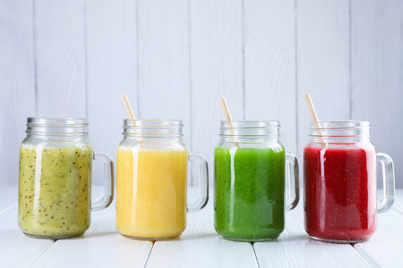 Different tasty smoothies in mason jars on white wooden tableの写真素材