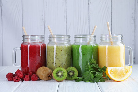 Different tasty smoothies in mason jars and ingredients on white wooden tableの写真素材