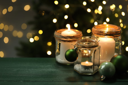 Beautiful Christmas lanterns and festive decor on green wooden table against blurred lights, space for text. Bokeh effectの写真素材