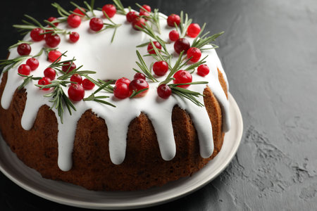 Tasty Christmas cake with icing, cranberries and rosemary on black table, closeupの写真素材