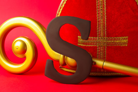 Saint Nicholas (Sinterklaas) day. Miter, crosier and chocolate letter S on red background, closeupの写真素材