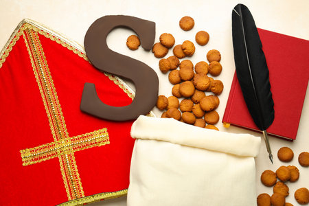 Sinterklaas (Saint Nicholas) Day. Chocolate letter S, kruidnoten cookies, mitre and notebook with feather on light background, flat layの写真素材