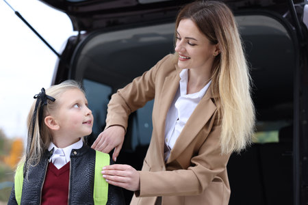 Mother taking her daughter to school near car outdoors