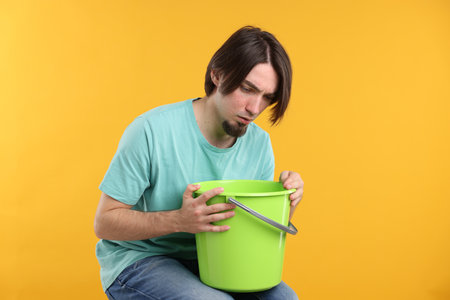 Man with bucket suffering from nausea on yellow backgroundの写真素材
