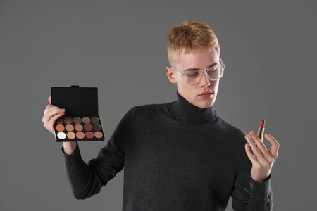 Makeup artist with eyeshadow palette and lipstick on gray backgroundの写真素材