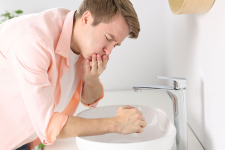Young man suffering from nausea over sink in bathroomの写真素材