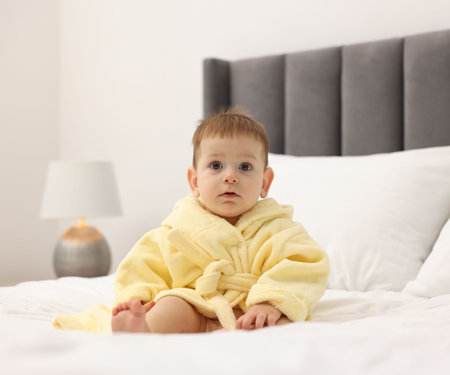 Cute baby in bathrobe on bed at homeの写真素材