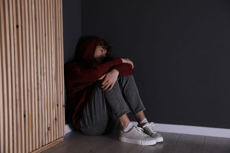 Depressed teenage boy near black wall indoors, space for textの写真素材