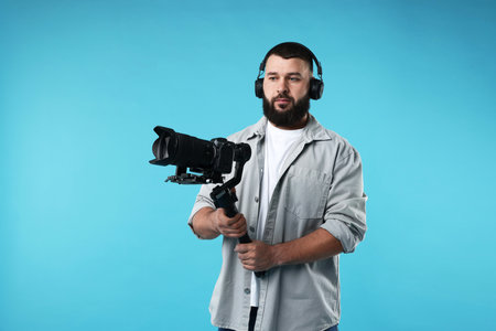 Videographer using gimbal stabilizer with camera on light blue background. Space for text