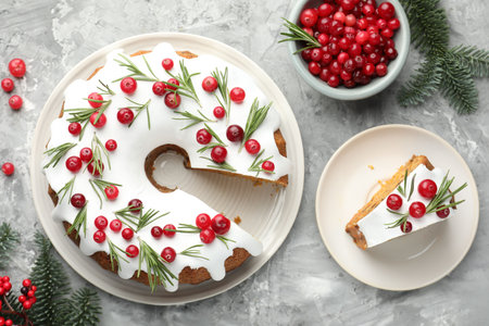Delicious cut Christmas cake with icing, cranberries, rosemary and fir tree branches on gray textured table, flat layの写真素材