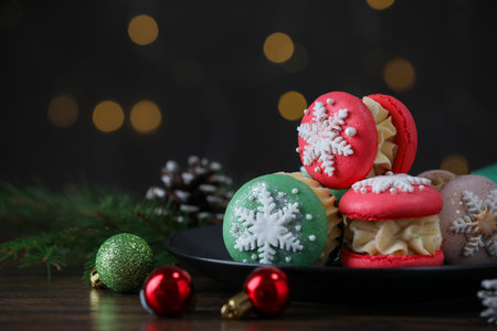 Tasty macarons and Christmas decor on black wooden table against blurred lights, closeup. Space for textの写真素材