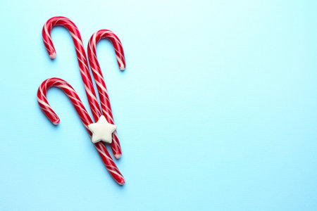 Tasty candy canes and gingerbread cookies on light blue background, flat lay with space for text.