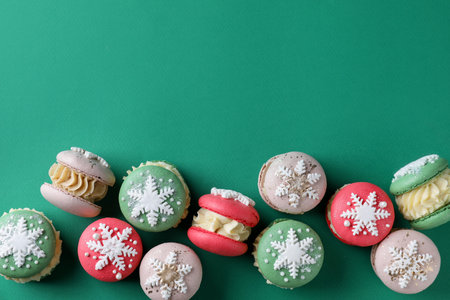 Beautifully decorated Christmas macarons on green background, flat lay. Space for textの写真素材