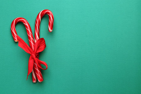 Tasty candy canes with bow on green background, top view with space for text. Merry Christmas and...