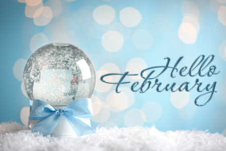 Hello February. Winter time card with snow globe against blurred lights on light blue backgroundの写真素材