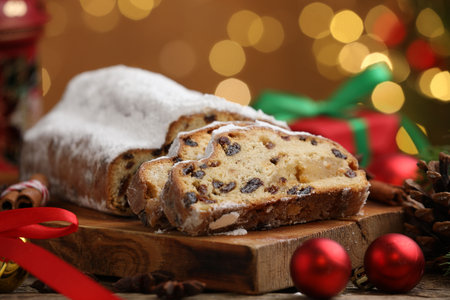 Traditional Christmas Stollen with icing sugar, spices and festive decor on wooden table against blurred lights, closeup. Bokeh effectの写真素材