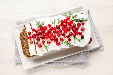 Tasty Christmas cake with icing, cranberries and rosemary on white wooden table, top view