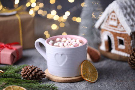 Tasty cocoa with marshmallows and Christmas decor on gray table against blurred lights, closeup