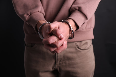 Man in handcuffs on black background, closeup