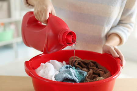 Woman pouring detergent into plastic basin with towels at table indoors, closeupの写真素材