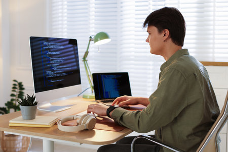 Programmer in headphones working on computer at table in officeの写真素材