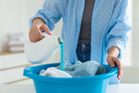 Woman pouring detergent into plastic basin with towels at table indoors, closeupの写真素材