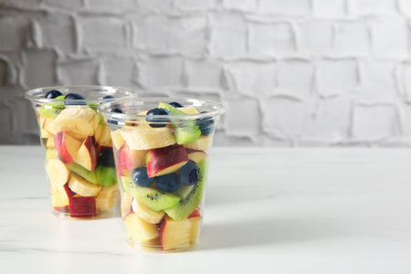 Tasty fruit salad in plastic cups on white marble table, closeup. Space for textの写真素材