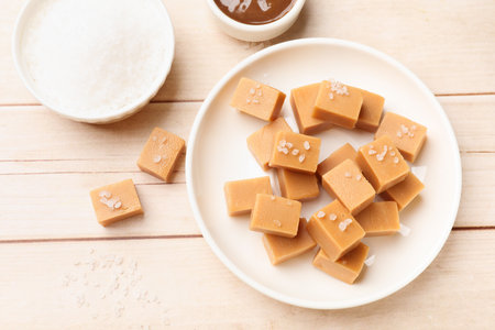 Tasty candies, salt and caramel sauce on light wooden table, flat layの写真素材