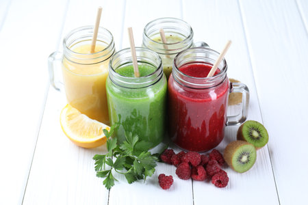 Different tasty smoothies in mason jars and ingredients on white wooden tableの写真素材