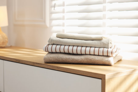 Stack of clean clothes on cabinet near window indoors, closeupの写真素材