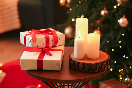 Burning candles and gift boxes on table near Christmas tree indoors, closeupの写真素材