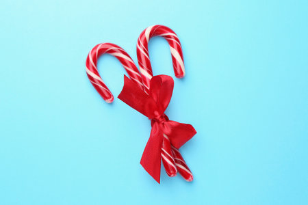 Tasty candy canes with bow on light blue background, top view. Merry Christmas and Happy New Year
