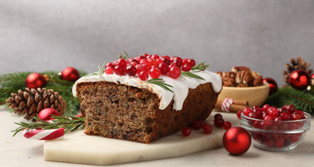 Tasty Christmas cake with icing, cranberries, nuts and festive decor on light gray table, closeup