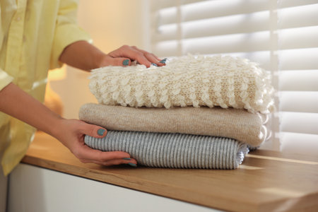 Woman with stack of clothes near window indoors, closeup