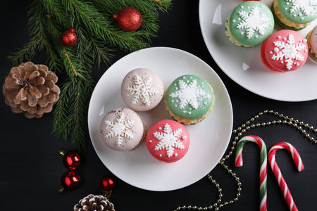 Tasty macarons and Christmas decor on black table, flat lay