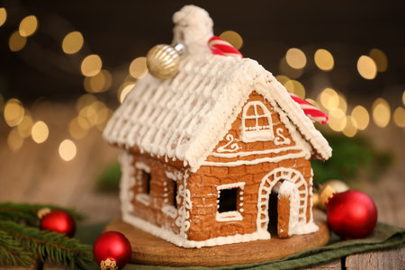 Beautiful gingerbread house and ornaments on wooden table against blurred lights, closeup. Christmas...