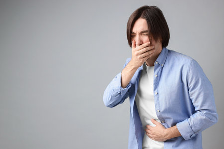 Man suffering from stomach ache and nausea on gray background. Space for textの写真素材