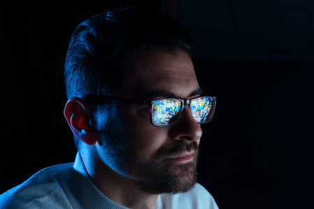 Man wearing glasses with reflection on black background in color light, closeup