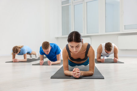 Group of people doing plank exercise on fitness mats in gym, selective focus
