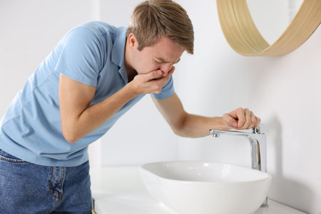 Young man suffering from nausea over sink in bathroomの写真素材