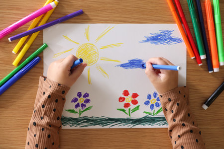 Cute little girl drawing with felt pen at wooden table, top view